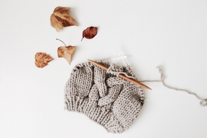 A knitted gray hat with knitting needles and dried leaves