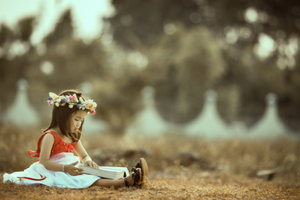 little girl wearing a flower crown, sitting on the ground reading a booking