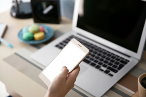 person holding a phone seated at a laptop