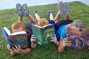 3 children lying on the grass reading books