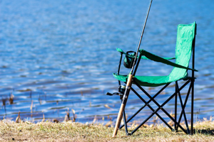 green lawn chair with fishing pole sitting by lake