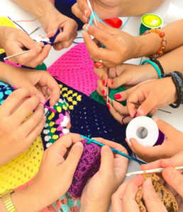 photograph of the hands of a number of people holding yarn and crochet hooks