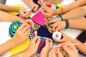 photograph of a number of hands holding yarn and crochet hooks